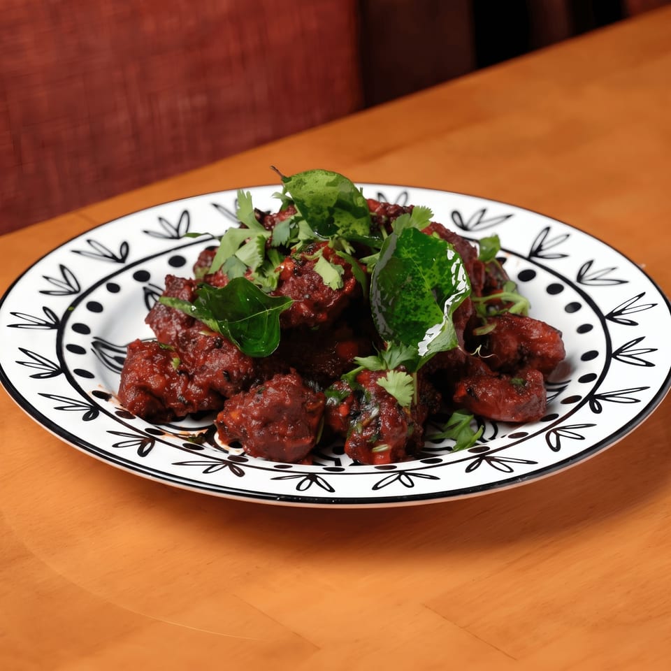 A plate of dark red, saucy chicken pieces garnished with fresh green herbs on a wooden table.