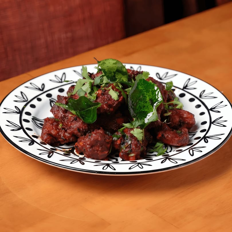 A plate of dark red, saucy chicken pieces garnished with fresh green herbs on a wooden table.