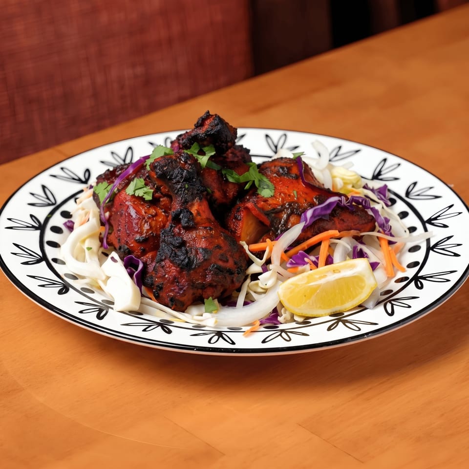 Tandoori chicken drumsticks with fresh cilantro, cabbage slaw, and a lemon wedge on a decorative plate.