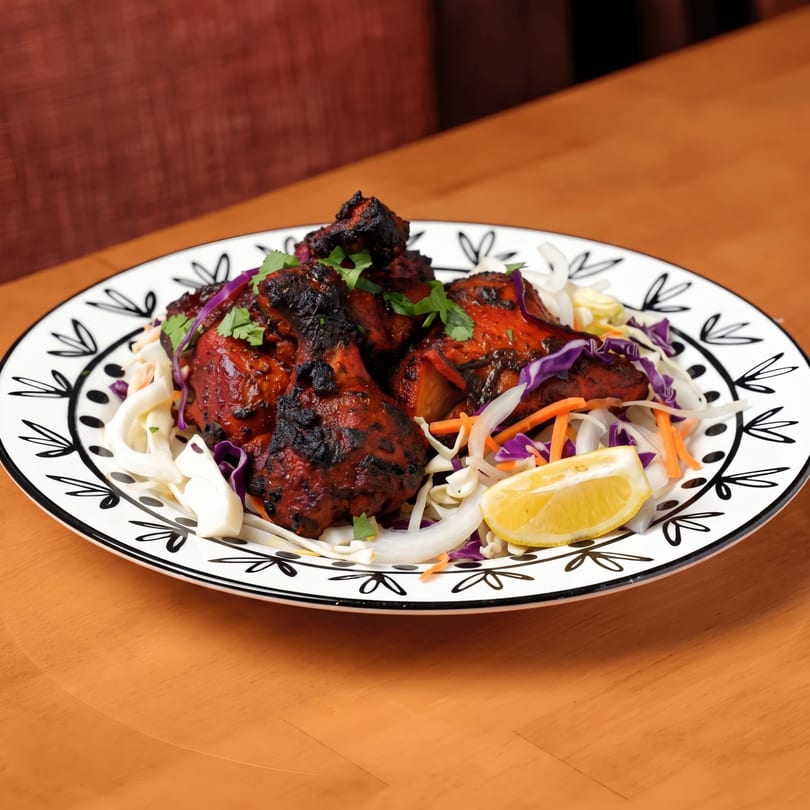 Tandoori chicken drumsticks with fresh cilantro, cabbage slaw, and a lemon wedge on a decorative plate.