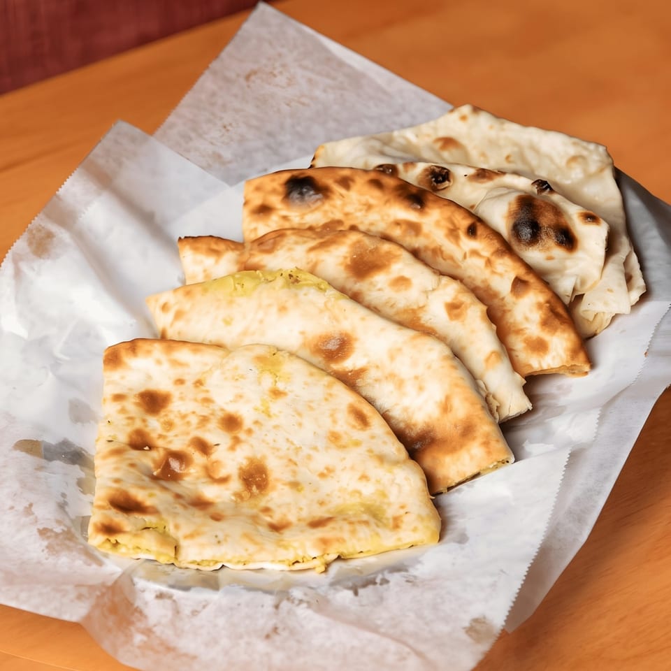 A basket of freshly baked naan bread, some plain and some stuffed, on white parchment paper.